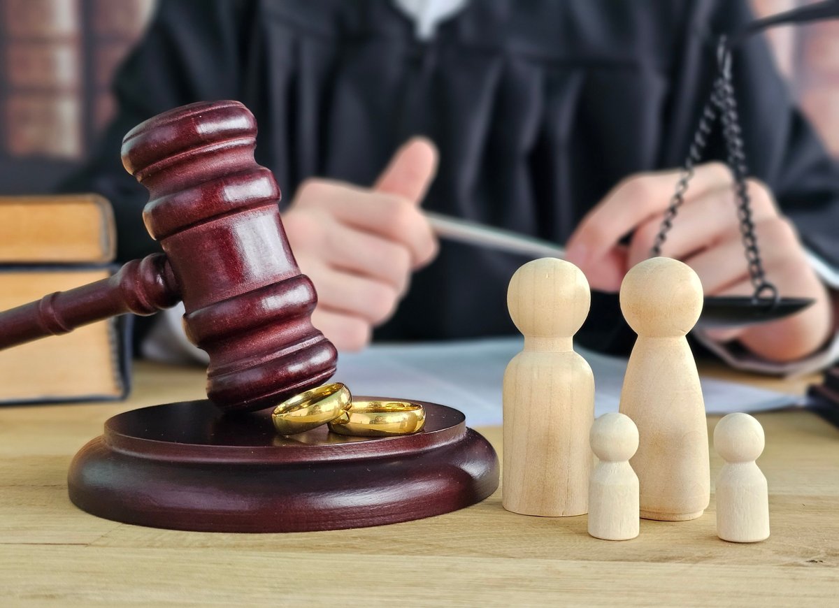 A gavel, small wooden figurines of parents and children, and a judge on a courtroom table with scales of justice