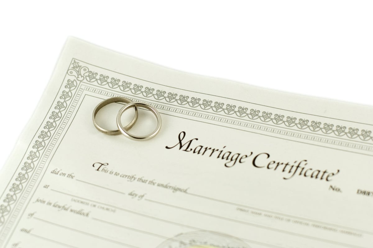 Two wedding rings resting on a marriage certificate with decorative border